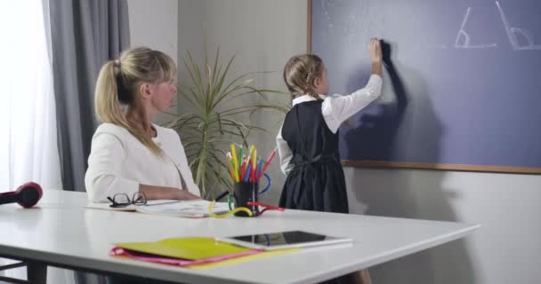 白人成人教师向黑板上书写的小女孩口述公式的肖像。 中年家庭教师在家里教孩子. 小学教育，勤奋，智慧。 电影4k Prores Hq. — 图库视频影像
