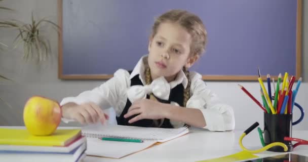 Charmig vit skolflicka skriver i träningsbok, biter äpple och visar tummen upp. Glad kvinnlig student som gör läxor. Utbildningskoncept, intelligens. Cinema 4k Prores Hq. — Stockvideo