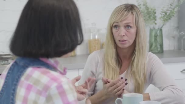 Portret van blonde slanke blanke vrouw luisterend naar brunette vrouwelijke vriend en gebaar. Vrouwen roddelen binnen. Vrije tijd, levensstijl, vriendschap. — Stockvideo