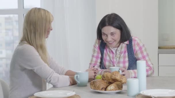 Porträt zweier erwachsener kaukasischer Frauen, die am Tisch sitzen und lächeln. Freunde, die zu Hause kommunizieren. Freundschaft, Lebensstil. — Stockvideo