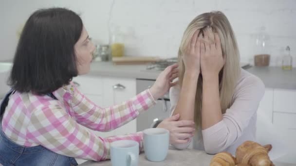 Retrato de una mujer caucásica adulta llorando sentada con la cara cerrada por las manos mientras su amiga la tranquiliza. Amistad para mujeres, apoyo, estilo de vida . — Vídeo de stock