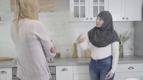 Kamera närmar sig Muselman kvinna i hijab argumentera med blond kaukasisk vän hemma. Två kvinnor grälar inomhus. Missförstånd, multietniska kommunikationsproblem. — Stockvideo