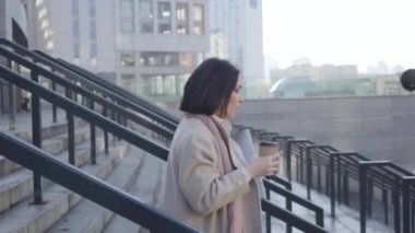 Kamera, elinde kahve fincanı, dosyasında belgelerle merdivenlerden inen esmer kadını takip ediyor ve saatine bakıyor. Genç beyaz iş kadını buluşmaya geç kaldı..