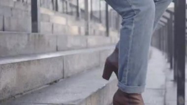 Beyaz kadın bacakları, ayak bileği ağrısı yüzünden merdivenlerden inip duruyor. Kot pantolonlu ve kahverengi çizmeli kadın hızlı bir yaşam sürmekten muzdarip. Sağlık, yaşam tarzı..