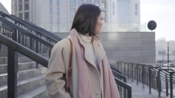 Retrato de una joven mujer caucásica de pie en las escaleras y esperando. Morena mujer de negocios en elegante abrigo beige mirando a su alrededor. Éxito, reuniones, estilo de vida . — Vídeo de stock