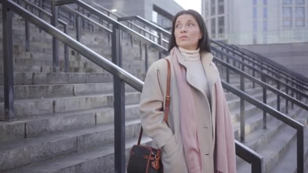 Portrait de jeune femme blanche brune debout sur les escaliers à l'extérieur et attendant quelqu'un. Femme d'affaires confiante regardant sa montre. Mode de vie, réunions, affaires . — Video