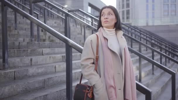 Portret van brunette Kaukasische jonge vrouw die buiten op de trap staat en op iemand wacht. Zelfverzekerde zakenvrouw die op haar horloge kijkt. Lifestyle, vergaderingen, zaken. — Stockvideo