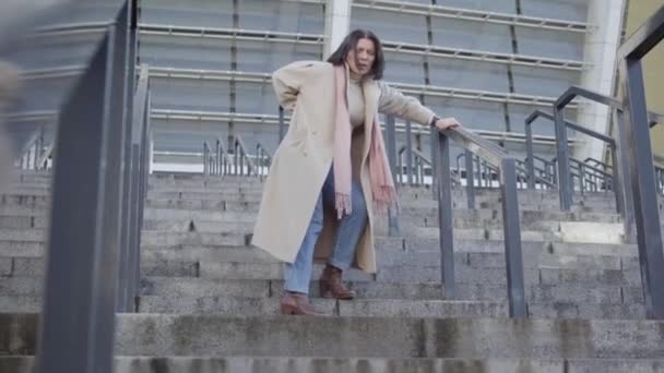 Joven hermosa mujer morena caucásica de pie en las escaleras y con la mano en la espalda. Elegante dama de negocios que se detiene por dolor de espalda. Trabajo duro, salud . — Vídeo de stock