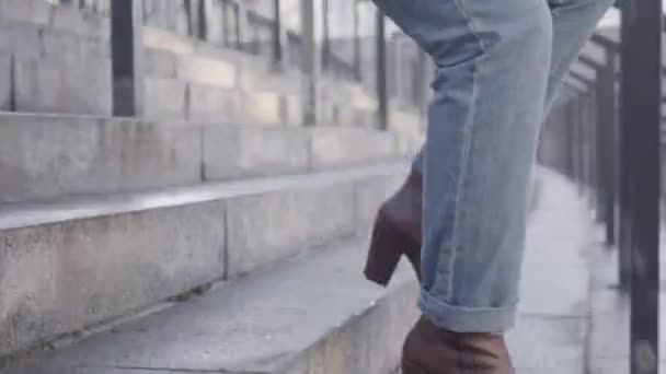 Vista lateral cercana de las piernas caucásicas femeninas bajando las escaleras y deteniéndose debido al dolor en el tobillo. Mujer en jeans y botas marrones sufriendo de ritmo rápido de vida. Asistencia sanitaria, estilo de vida . — Vídeo de stock