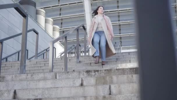 Egy fiatal, vonzó kaukázusi nő portréja, amint sétál lefelé a lépcsőn, amikor éles bokafájdalmai vannak. Fiatal, gyönyörű üzletasszony szenved a magassarkú miatt. Keményen dolgozó, túlhajszolt, egészségügyi. — Stock videók