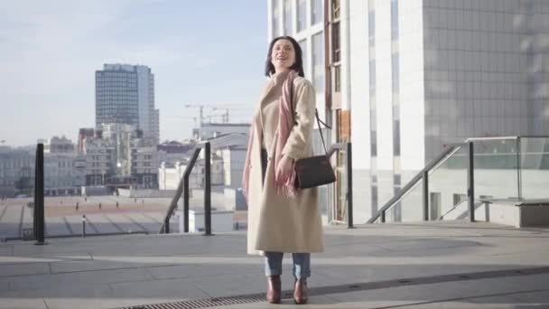 Portret białej kobiety cieszącej się słonecznym dniem, stojącej na ulicy miejskiej. Młoda bizneswoman brunetka stojąca na tle drapaczy chmur i uśmiechnięta. Styl życia, duma, sukces, szczęście. — Wideo stockowe