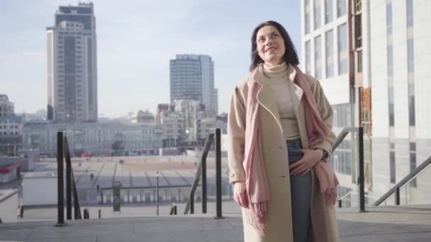 Весела кавказька жінка стоїть у місті в сонячний осінній день і посміхається. Позитивна жінка проводить сонячний день у місті. Спосіб життя, гордість, успіх. — стокове відео