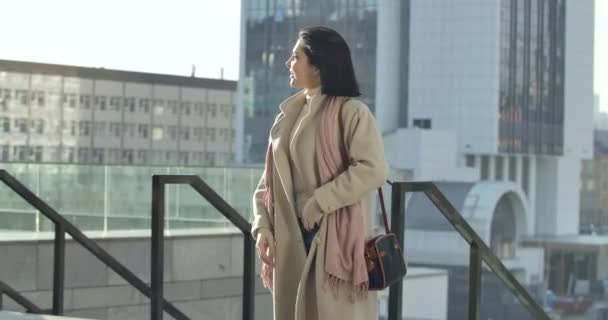 Mujer positiva caucásica disfrutando de un día soleado en la ciudad. Morena mujer de negocios de pie en el fondo de los rascacielos y sonriendo. Estilo de vida, orgullo, éxito. Sede del cine 4k ProRes . — Vídeo de stock