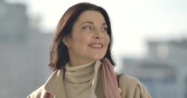 Close-up face of beautiful smiling Caucasian woman standing outdoors. Brunette young lady in beige outfit enjoying sunny day. Cinema 4k ProRes HQ. — Stock Video