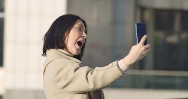 Portret van een blanke zakenvrouw die buiten een videogesprek heeft. Jonge zelfverzekerde vrouw die smartphone gebruikt, praat en lacht alsof ze op straat staat. Bioscoop 4k Prores Hq. — Stockvideo