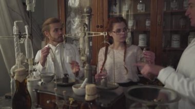Üç beyaz eczacının portresi konuşuyor. Antik eczanelerde deney tüpleri, mataralar ve antika kimyasal konteynırlarla duran insanlar. Şişelere yazılan kimyasal terimler.