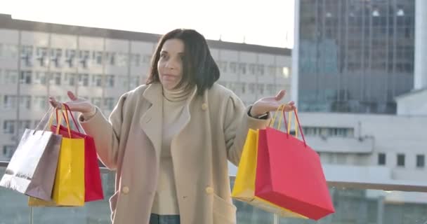 Portret van een blanke vrouw die kleurrijke boodschappentassen opvoedde en lachte. Volwassen vrouwelijke shopaholic staan op straat met aankopen. Shopaholisme, levensstijl. Bioscoop 4k Prores Hq. — Stockvideo