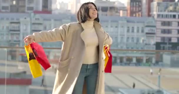 Alegre mujer caucásica bailando con coloridas bolsas de compras y cantando. Feliz adicto a las compras disfrutando de compras en la calle de la ciudad. Compras, estilo de vida. Sede del cine 4k ProRes . — Vídeo de stock