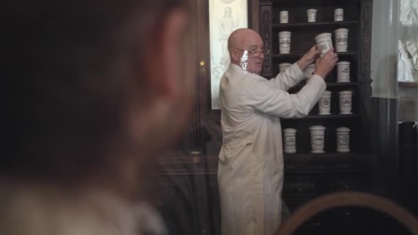Pozitivní zralý kavkazský lékárník, který bere staromódní obal s léky a přichází k pokladně. Starý lékárník pomáhá zákazníkovi vybrat si lék. Ročník, retro, 19. století. — Stock video