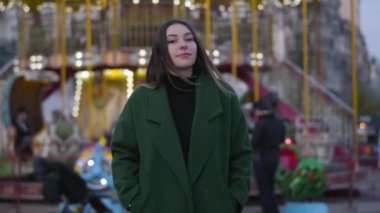 Renkli atlıkarıncaların önünde duran güzel beyaz kıza yavaşça yaklaşan kamera. Genç ve güzel bir kadın kameraya bakıyor ve gülümsüyor. Yaşam tarzı, mutluluk, rahatlık.