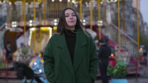 Macchina fotografica che si avvicina lentamente a di bella ragazza caucasica in piedi di fronte a giostre colorate. Giovane bella donna guardando la fotocamera e sorridendo. Stile di vita, felicità, tempo libero . — Video Stock