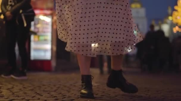 Female Caucasian legs in light skirt and boots spinning, camera moving up to face of beautiful girl in pink hat. Young pretty woman having fun on city market in the evening, Lifestyle, leisure. — Stock Video