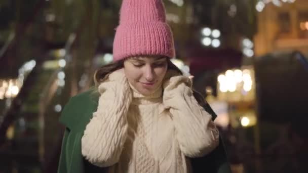 Retrato de niña caucásica en sombrero rosa y abrigo verde de pie en el fondo del carrusel. Mujer linda joven pasar tiempo libre en el mercado de la ciudad. Estilo de vida, ocio, felicidad . — Vídeos de Stock