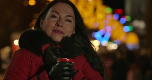 Gros plan de la charmante femme caucasienne debout avec tasse de café, regardant la caméra et souriant. Belle dame d'âge moyen debout sur le marché de la ville à l'arrière-plan de carrousels. Siège social Cinema 4k ProRes . — Video