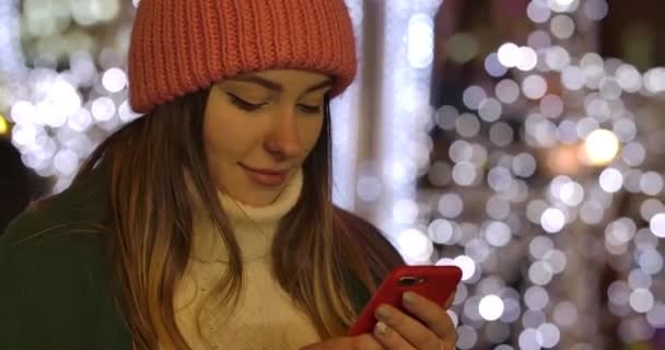 穿着冬季服装的可爱白人女孩用智能手机和微笑的特写。 年轻美丽的女人在户外消磨时光。 电影4k Prores Hq. — 图库视频影像