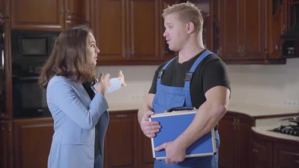 Jeune femme caucasienne et réparateur rousse en peignoir debout à la cuisine et parler. Propriétaire de la maison expliquant au travailleur le problème qu'il doit résoudre. Professionnel, réparation, travail . — Video