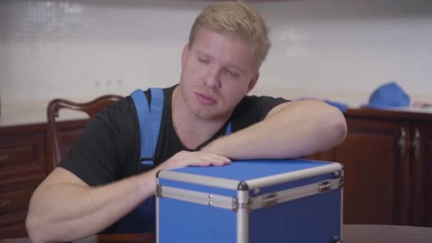 Porträtt av utmattad vit reparatör som somnar på arbetsplatsen. Ung rödhårig man lägger huvudet på verktygslådan och sover. Trötthet, yrke, överarbete. — Stockvideo
