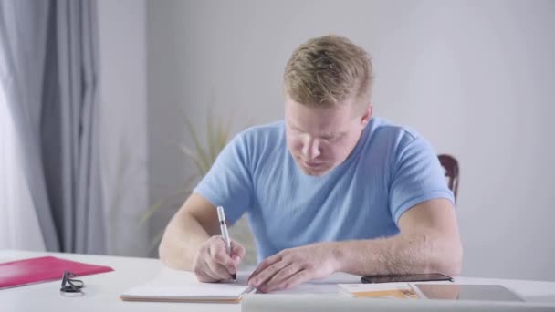 Zelfverzekerde blanke zakenman die aan tafel zit en aantekeningen maakt. Een roodharige man die binnen aan zijn nieuwe ideeën denkt. Lifestyle, intelligentie, zaken doen. — Stockvideo