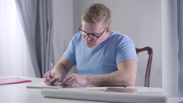 Portrait d'un homme d'affaires caucasien confiant portant des lunettes assis à la table et prenant des notes. Un rouquin réfléchissant à ses nouvelles idées à l'intérieur. Mode de vie, intelligence, affaires . — Video