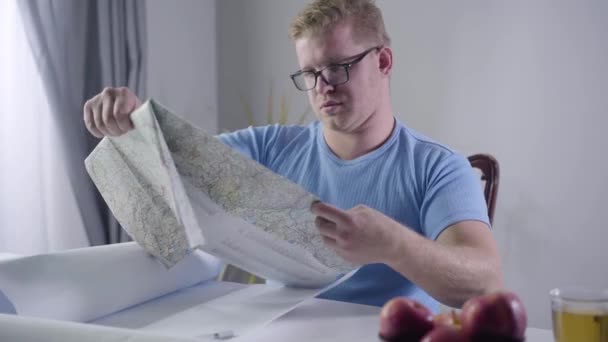 Caméra approchant de rousse Architecte caucasien en lunettes assis à la table avec carte et plans. Designer professionnel travaillant à l'intérieur. Professionnel, profession, travail, style de vie . — Video