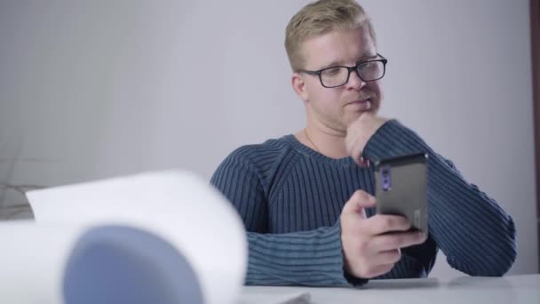 Retrato de empresário caucasiano inteligente em óculos sentado à mesa com smartphone. Retrato de homem confiante no escritório. Trabalho, profissão, profissão . — Vídeo de Stock