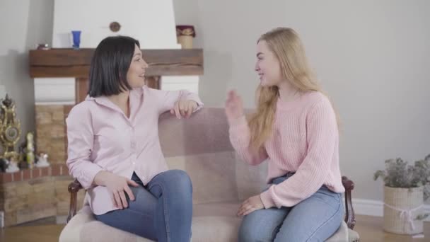 Retrato de madre caucásica e hija adulta sentada en el sofá, hablando y riendo. Positiva chica adolescente divirtiéndose con mamá en casa. Relación, familia, felicidad . — Vídeos de Stock