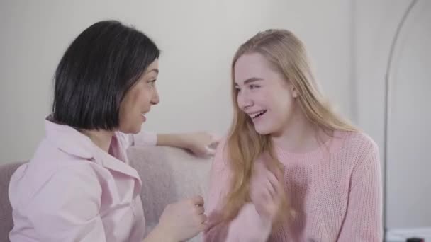 Retrato de mujer y niña caucásicas sentadas en el sofá hablando y riendo. Alegre hija adolescente divirtiéndose con la madre en casa. Relación, familia, felicidad . — Vídeos de Stock