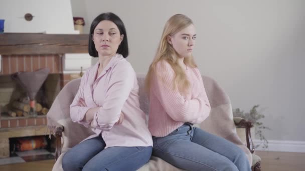 Widok z boku dorosłej białej brunetki i nastolatki siedzącej z tyłu na sofie. Matka i córka się kłóciły. Relacje rodzinne, konflikt, problemy. — Wideo stockowe
