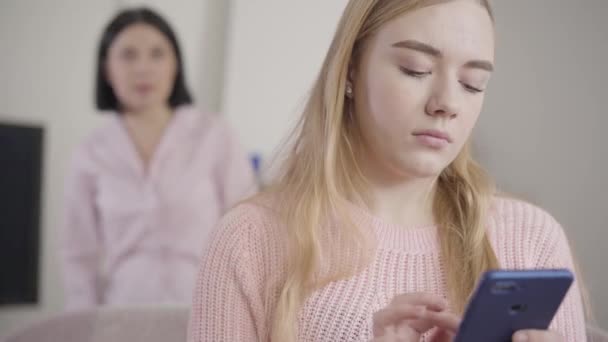 Närbild av brunett vit kvinna som kommer från bakgrunden och ta bort döttrar smartphone. Mor grälar med tonårstjejen hemma. Missförstånd, konflikt, generationer. — Stockvideo