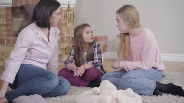 Porträtt av lycklig vit familj som sitter på mjuk matta framför öppen spis och pratar. Mor umgås med två döttrar hemma. Fritid, livsstil, lycka. — Stockvideo