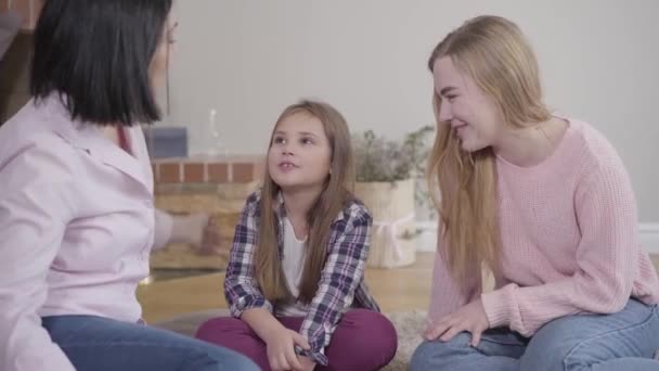 Porträtt av söt vit tjej som sitter på mjuk matta och leker med mamma och syster. Barn tillbringar tid med familjen hemma. Fritid, livsstil, lycka. — Stockvideo