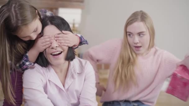 Twee blanke dochters die hun schattige moeder een verrassing geven. Gelukkige brunette die thuis een cadeau krijgt. Geluk, vrije tijd, levensstijl. — Stockvideo