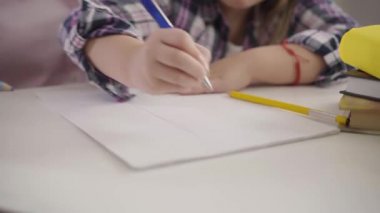 Küçük çocukların ellerinin egzersiz kitabına çizgiler çizdiği yakın plan. Öğrenci kız masada oturuyor ve ödev yapıyor. Eğitim, el yazısı.