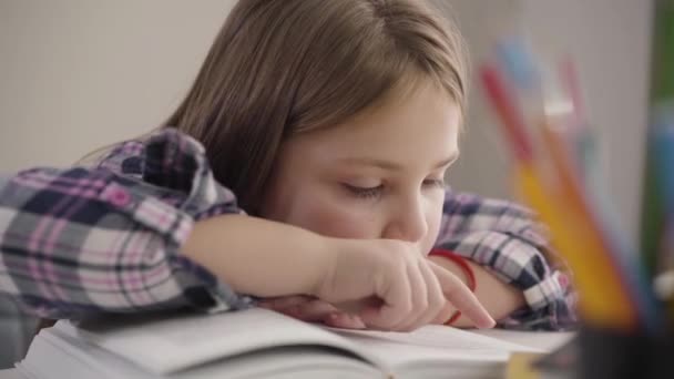 Porträtt av söt brunett vit flicka läser bok vid bordet. Närbild av skolbarn som gör läxor hemma. Utbildning, intelligens, studier. — Stockvideo