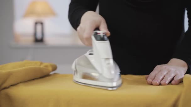 Primer plano de las manos femeninas planchando suéter amarillo. Joven ama de casa musulmana haciendo tareas domésticas. Europa central y oriental, sociedad moderna . — Vídeo de stock