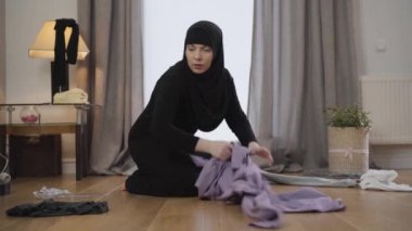 Doğulu genç ev hanımı portresi yerden kıyafet topluyor. Çaresiz Müslüman kadın ev işi yapıyor. Geleneksel kültür, ev idaresi.