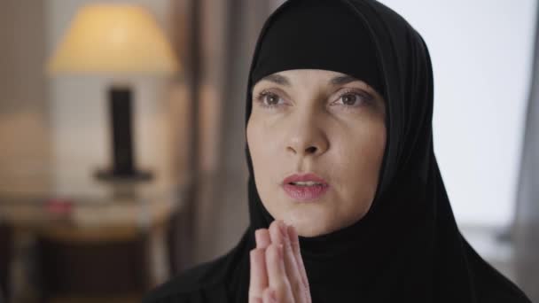 Gros plan sur le visage d'une jeune belle musulmane tenant la main et priant. Dame en hijab traditionnel noir parlant avec Dieu. Culture, religion. Caméra se déplaçant de droite à gauche . — Video