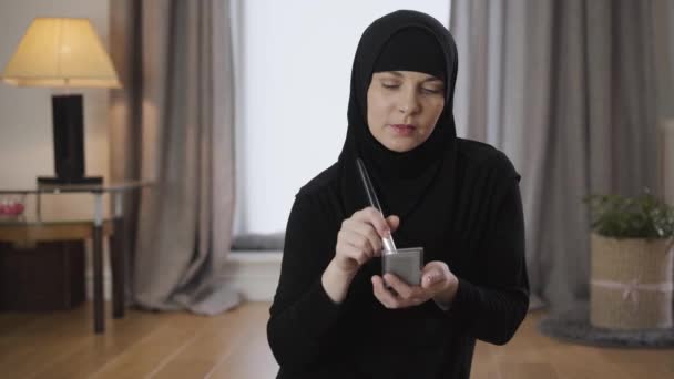 Porträtt av attraktiv muslimsk kvinna applicera ansiktspulver. Leende söt dam i hijab som sminkar sig hemma. Modern österländsk kultur, skönhet. — Stockvideo