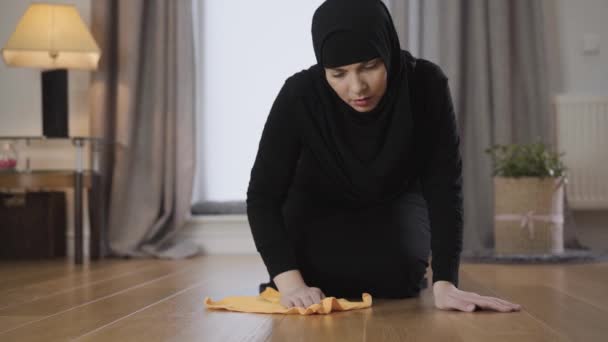 Närbild av ung Muselman dam i hijab rengöring golv med gul trasa. En flitig hemmafru som blåser på golvet och torkar. Hushållsskötare, hushållsarbete. — Stockvideo