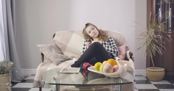 Portrait of teen Caucasian girl sitting on couch and watching TV. Pretty young lady watching movies or series at home on weekends. Adolescence, lifestyle. Cinema 4k ProRes HQ. — 비디오
